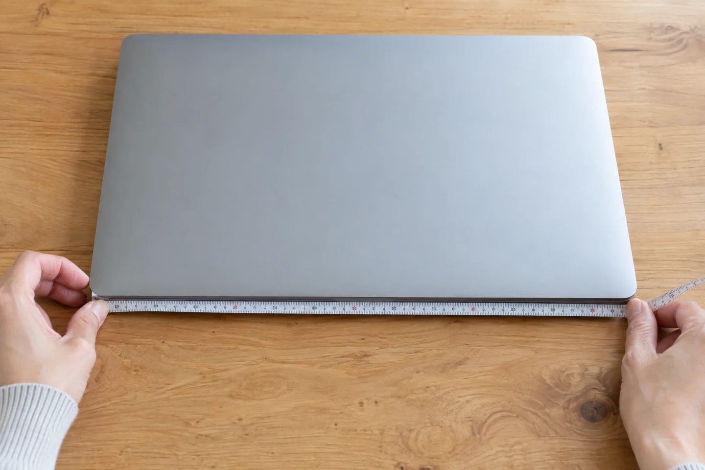閉じたノートPCの外側にメジャーを当てたイメージ